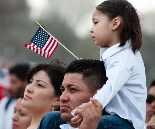 A little girl on her dad's shoulder with the American flag