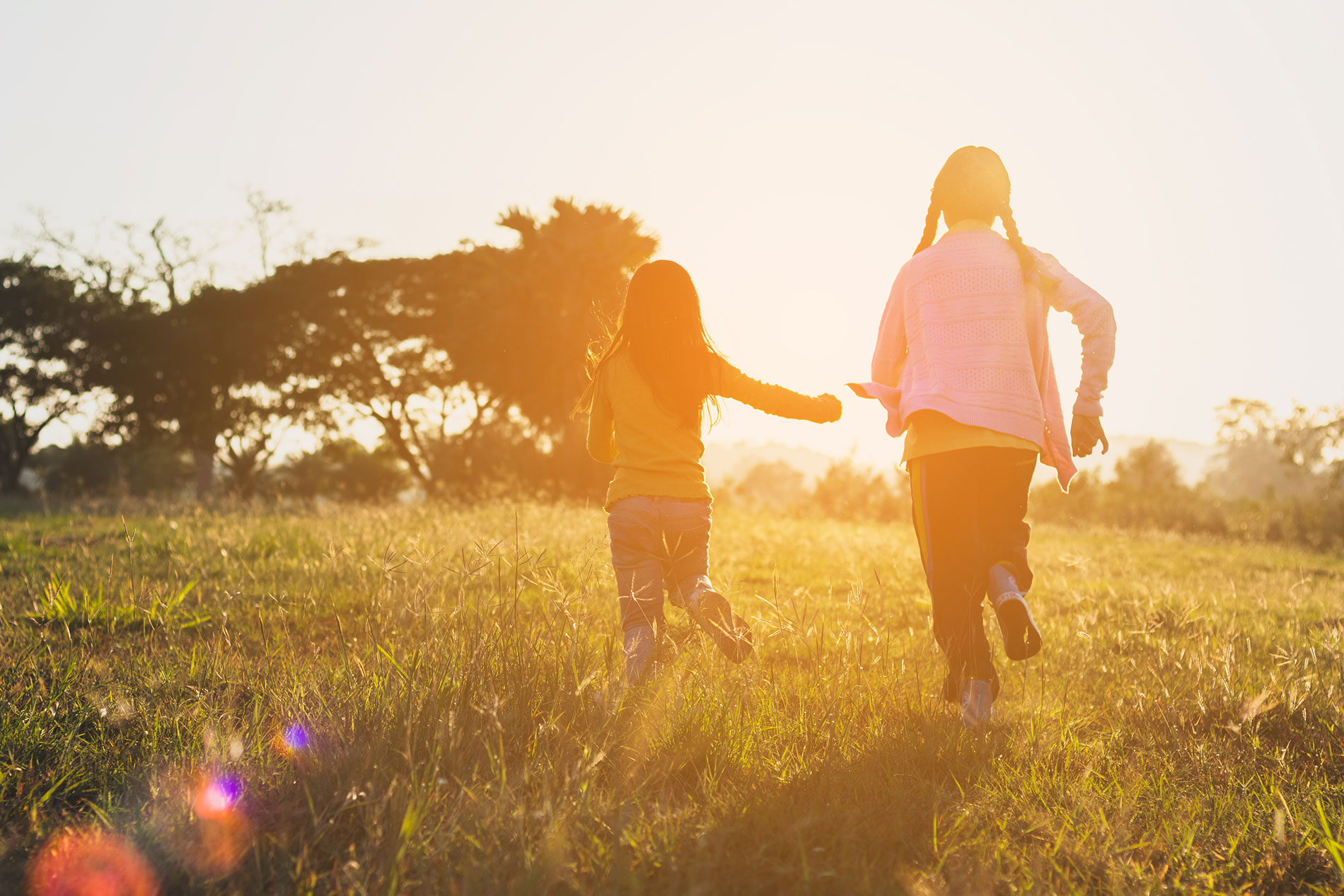 Two girls running in a field at sunset