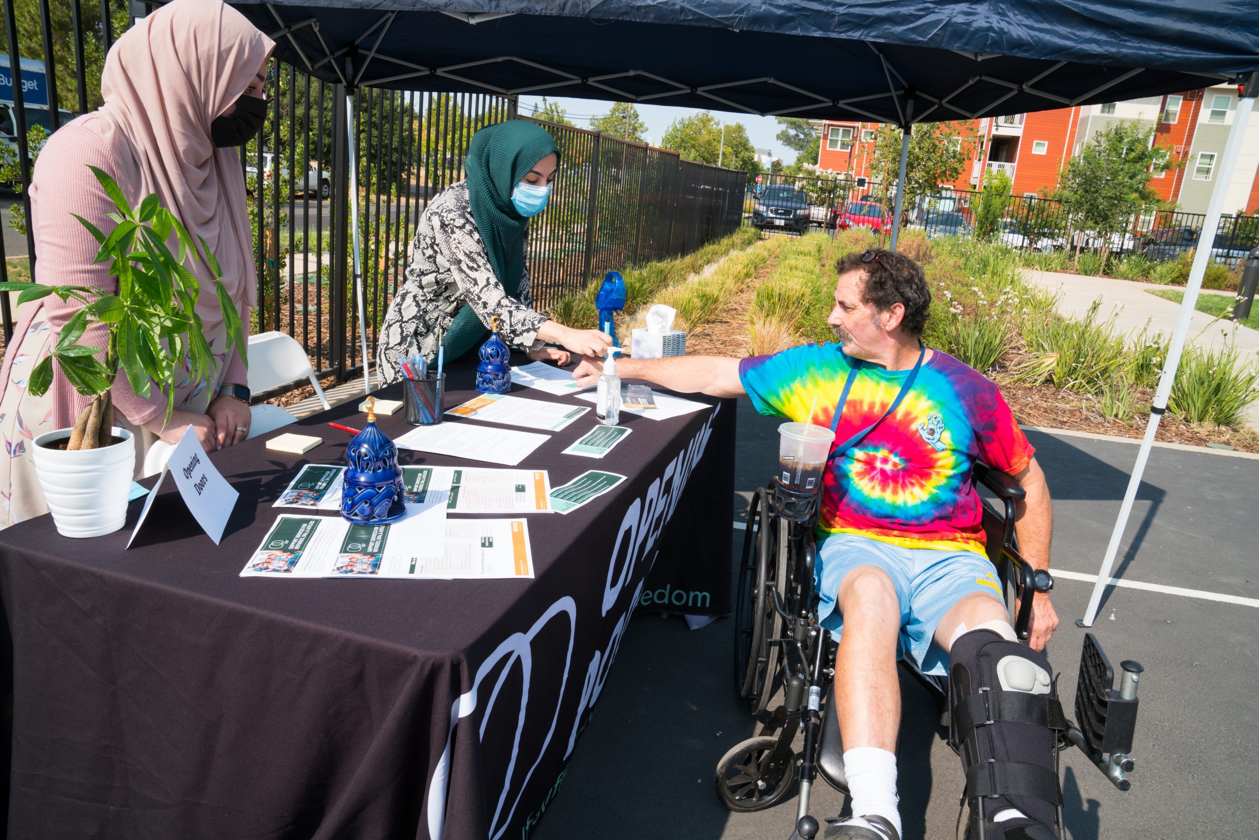 A man in a wheelchair receiving program information from two Opening Doors volunteers
